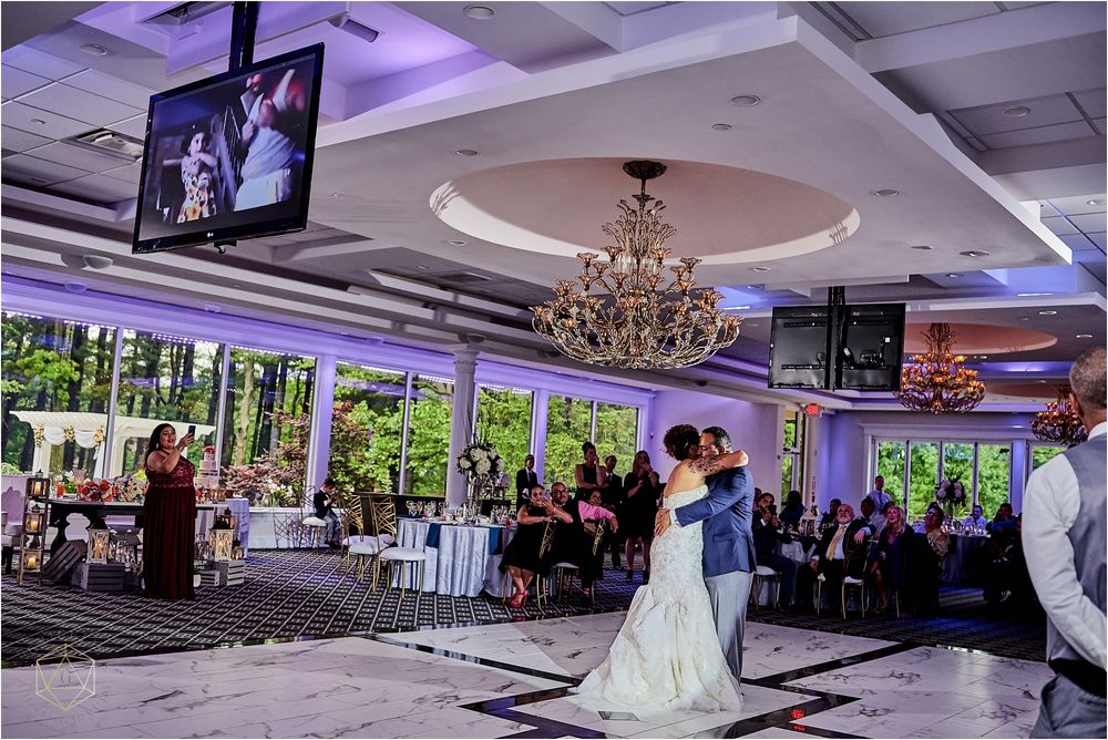 Wedding reception ballroom with crystal chandelier and video screens showing the celebration.