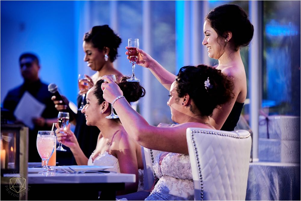 Bridesmaids in formal attire raise glasses for a toast at an elegant wedding reception.