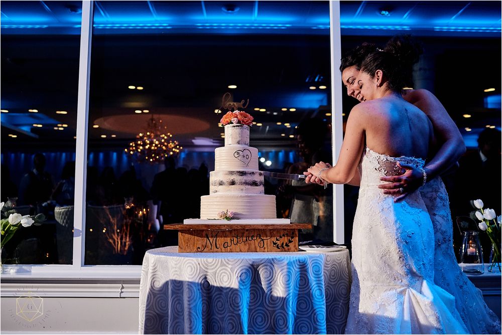 Elegant white wedding cake display with couple standing beside it at reception venue.