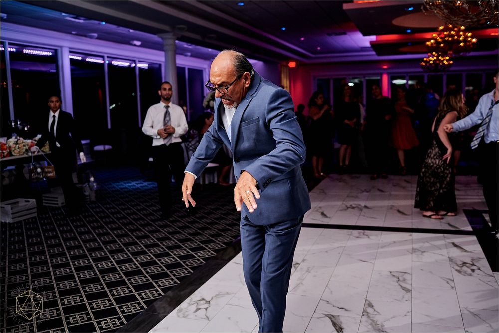 Guest in blue suit dances enthusiastically on patterned floor at wedding reception.