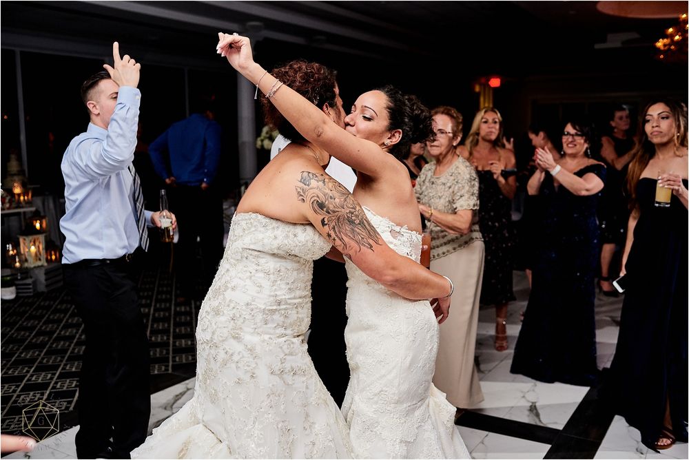 Wedding celebration with guests dancing in formal attire on black and white checkered floor.