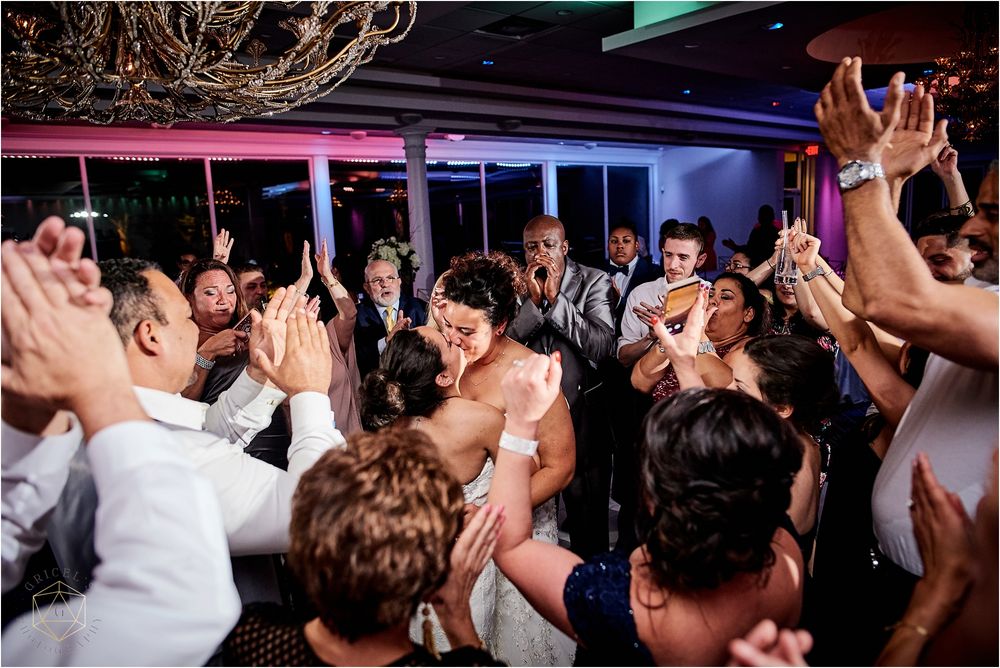 Energetic dance party scene at wedding reception with crowd raising hands in celebration.