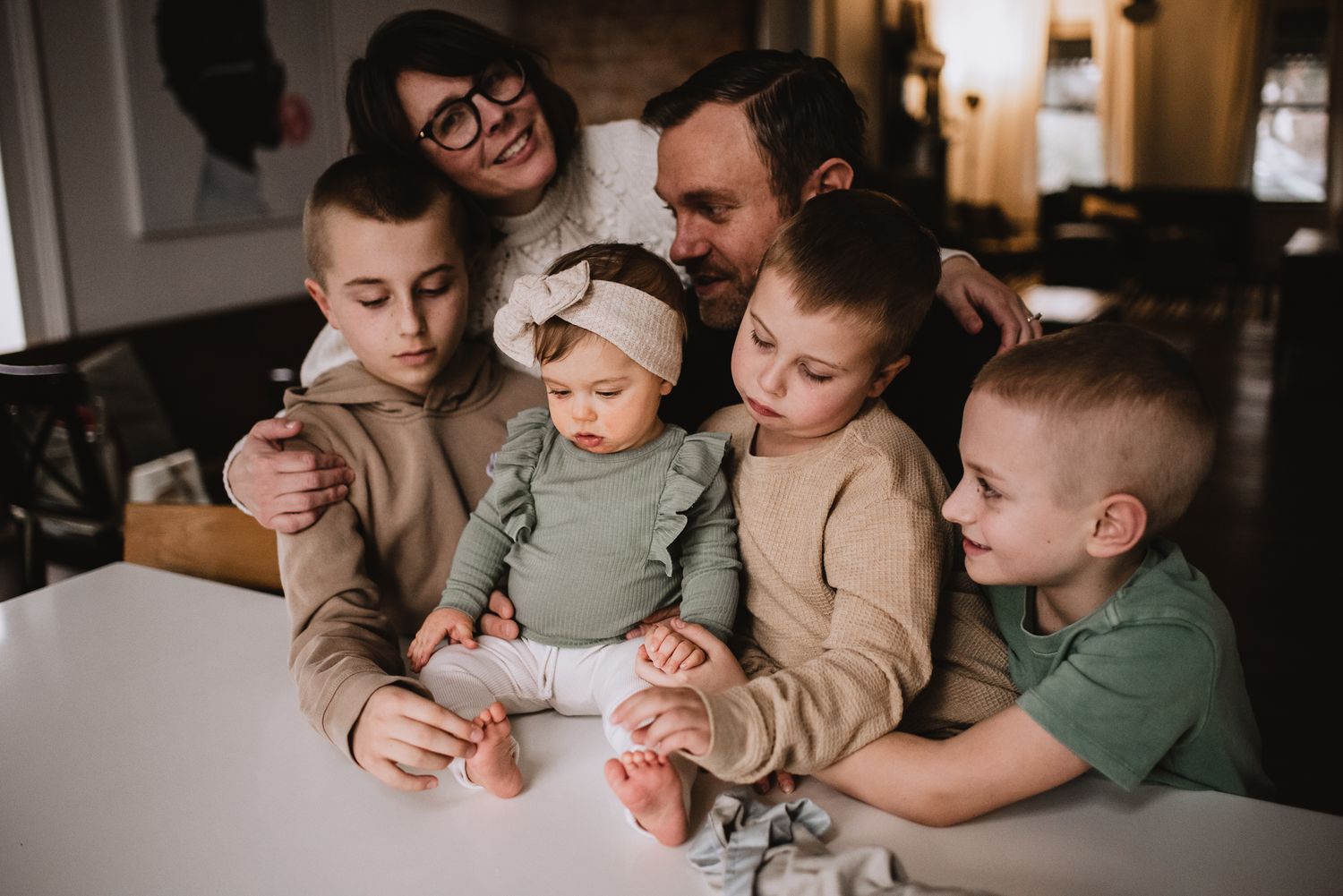 Cozy family moment gathered around a white table sharing attention on something together.