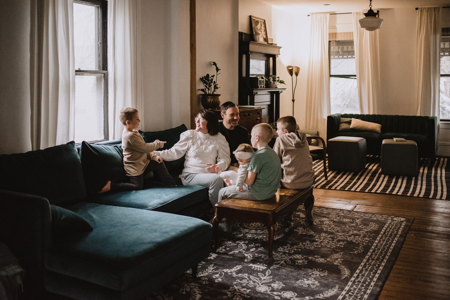 A cozy living room scene with people relaxing on a blue sectional sofa beneath large windows.