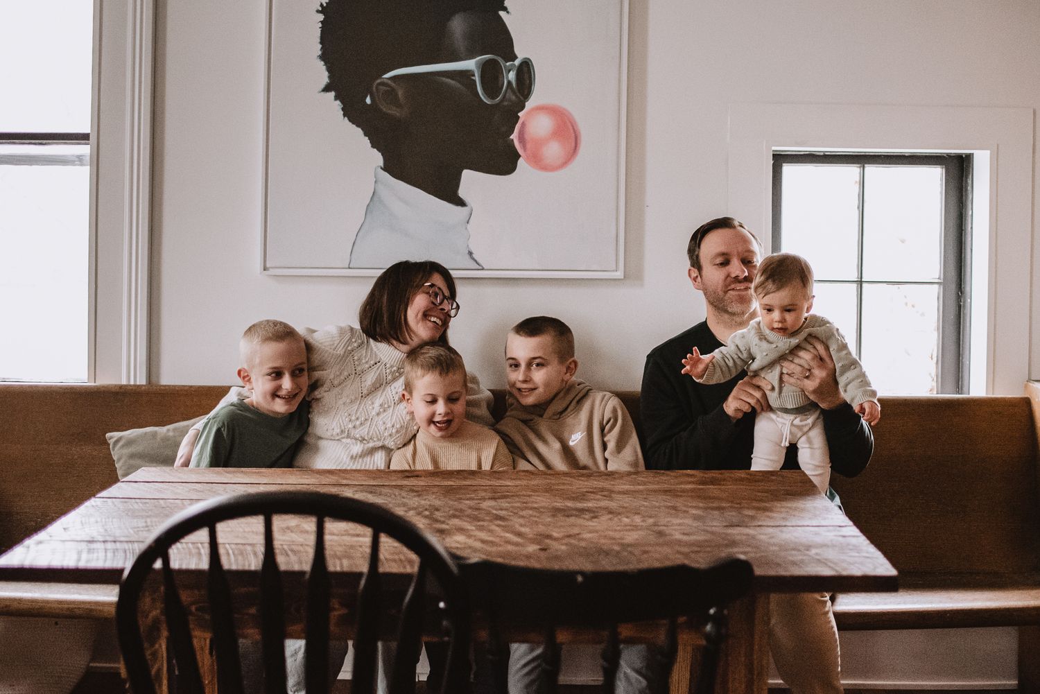 A family gathering around a wooden table with modern art on the wall behind them.