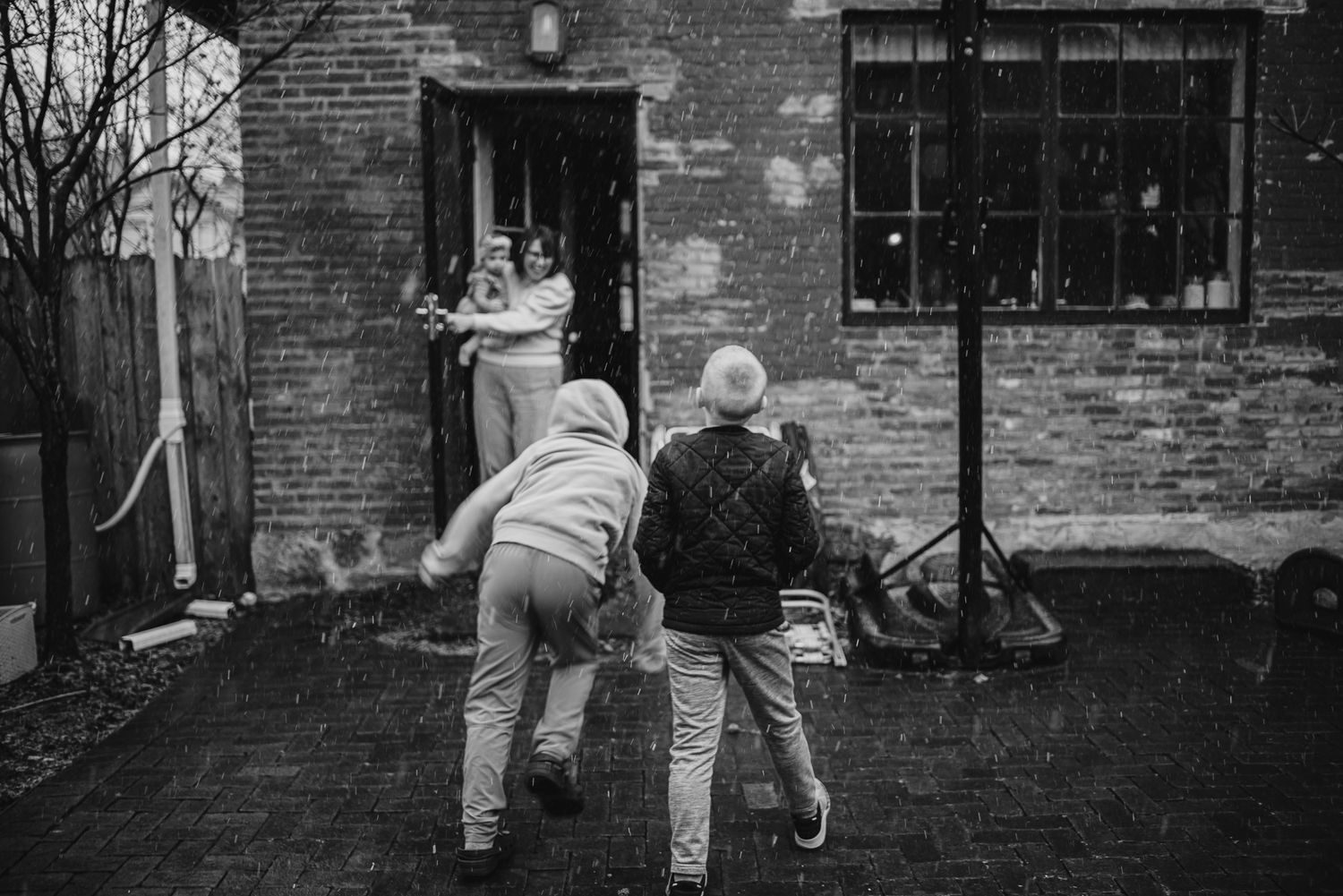 Two figures running and playing together outside a brick building on a rainy day.