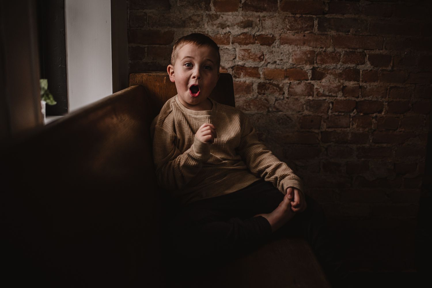 A candid moment showing joyful expression against a rustic brick wall backdrop in moody lighting.