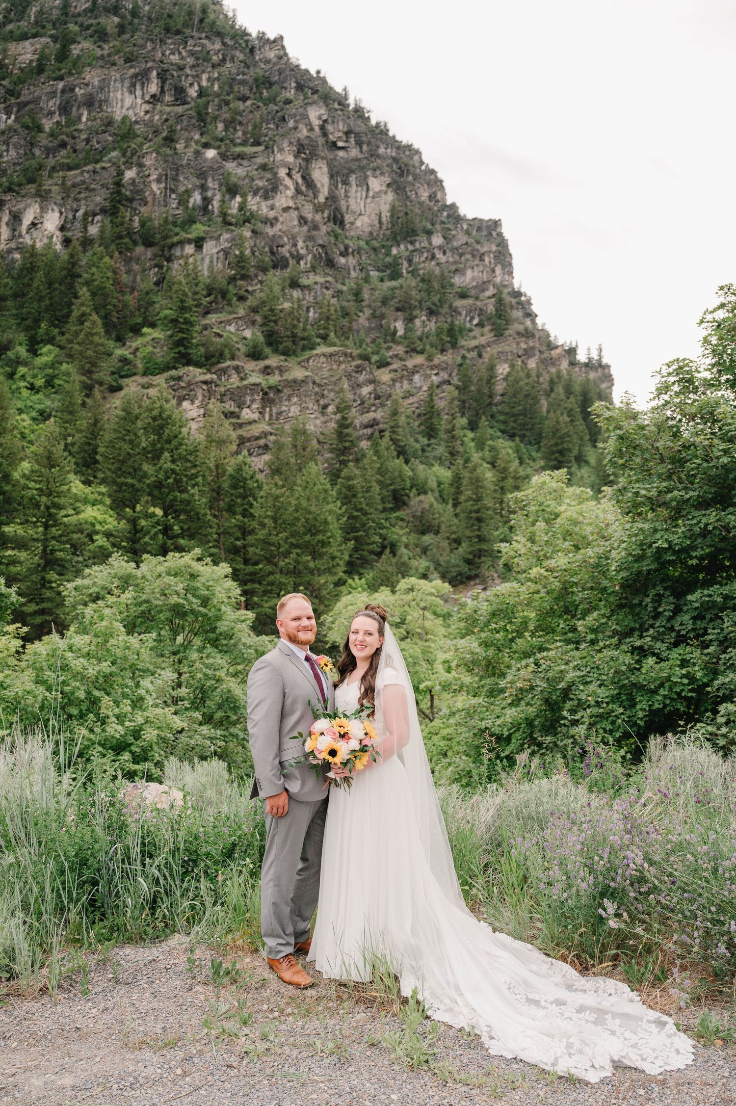 Wedding portrait with dramatic mountain cliffs and evergreen forest creating a majestic backdrop.