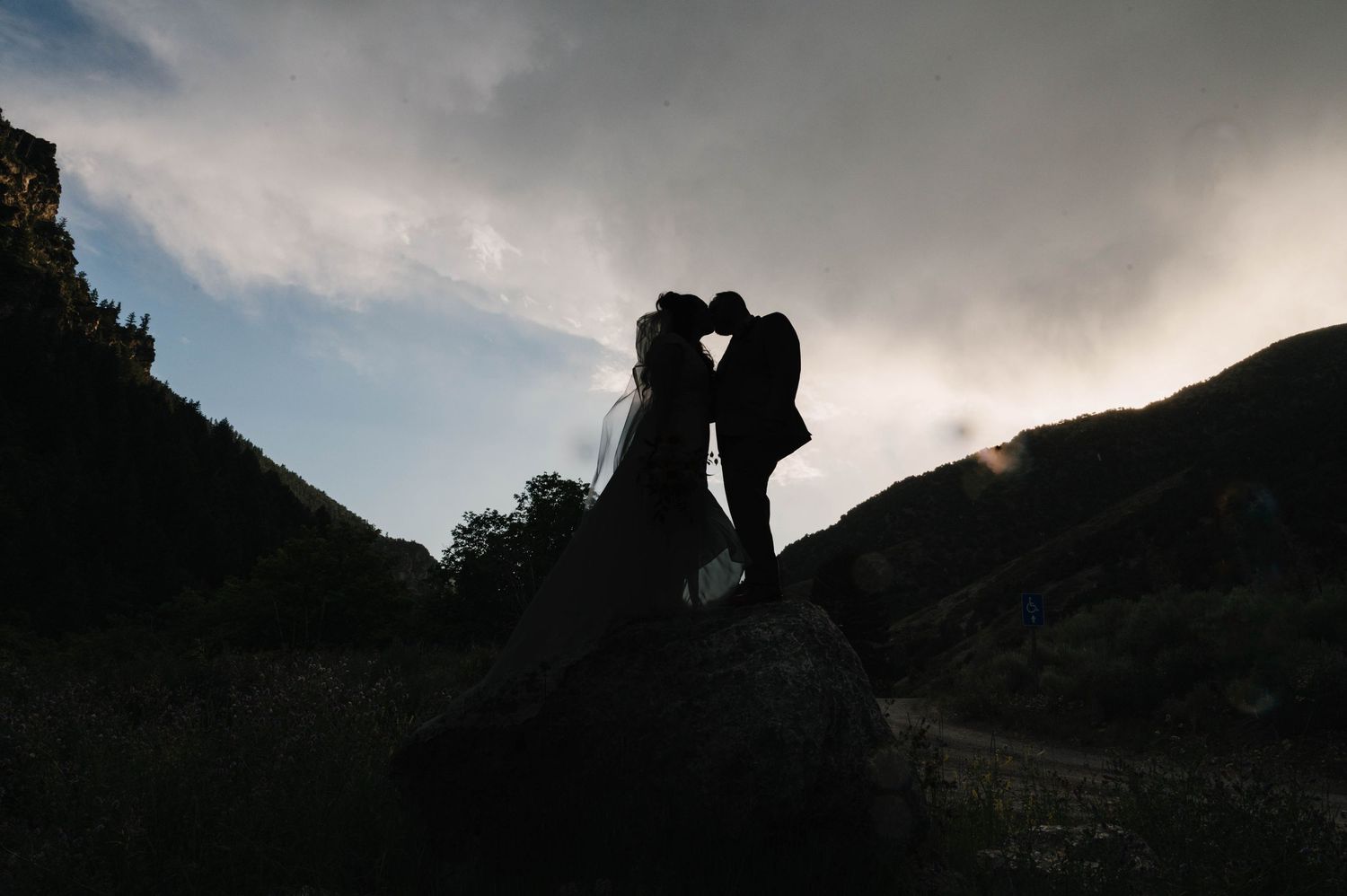 Silhouette of a couple embracing on a mountaintop at sunset.