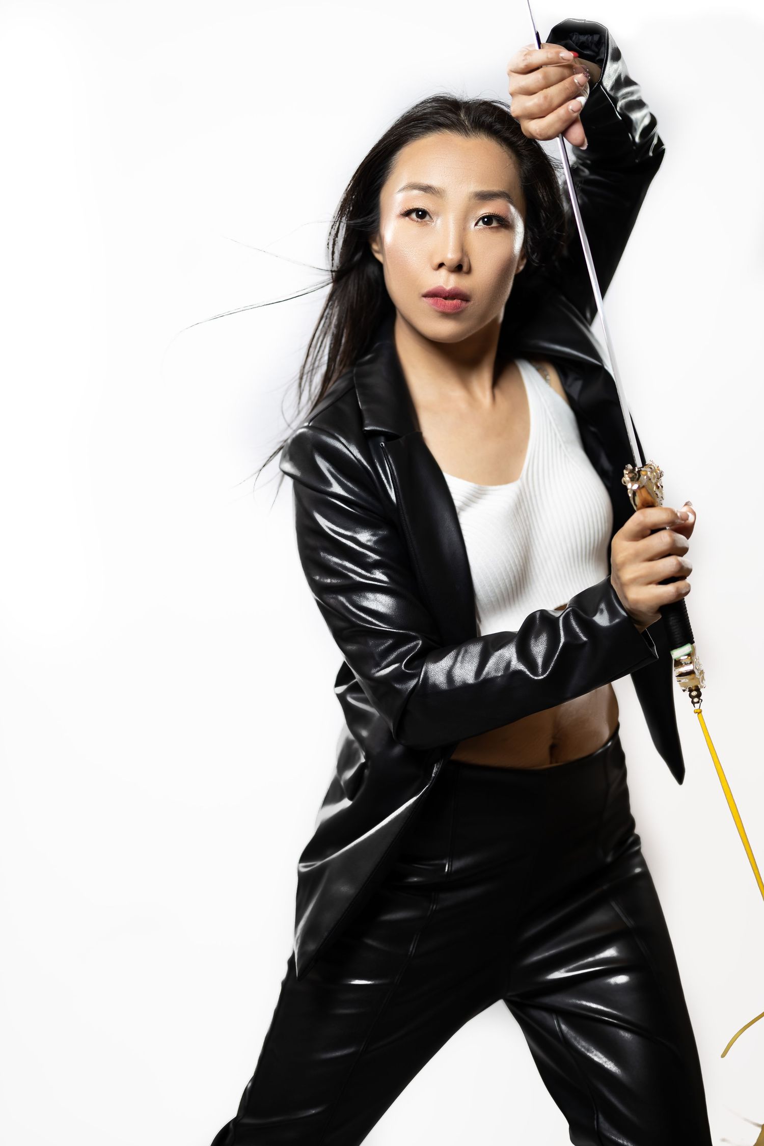 Dynamic pose with sword in sleek black leather outfit against white background.