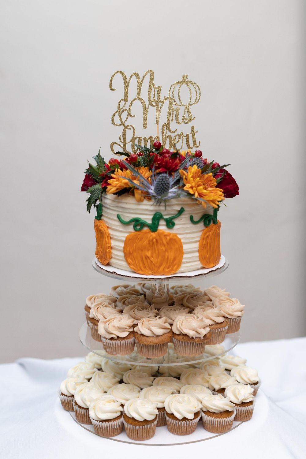 Fall-themed wedding cake with pumpkins and flowers on a tiered cupcake display stand.