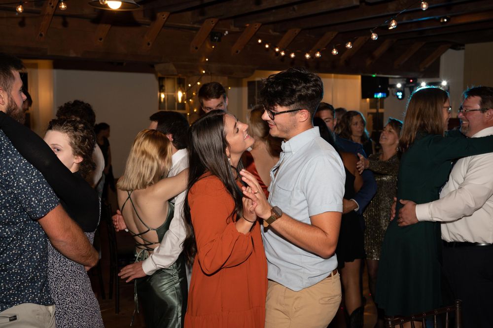 Party guests dancing together under string lights at an indoor venue.