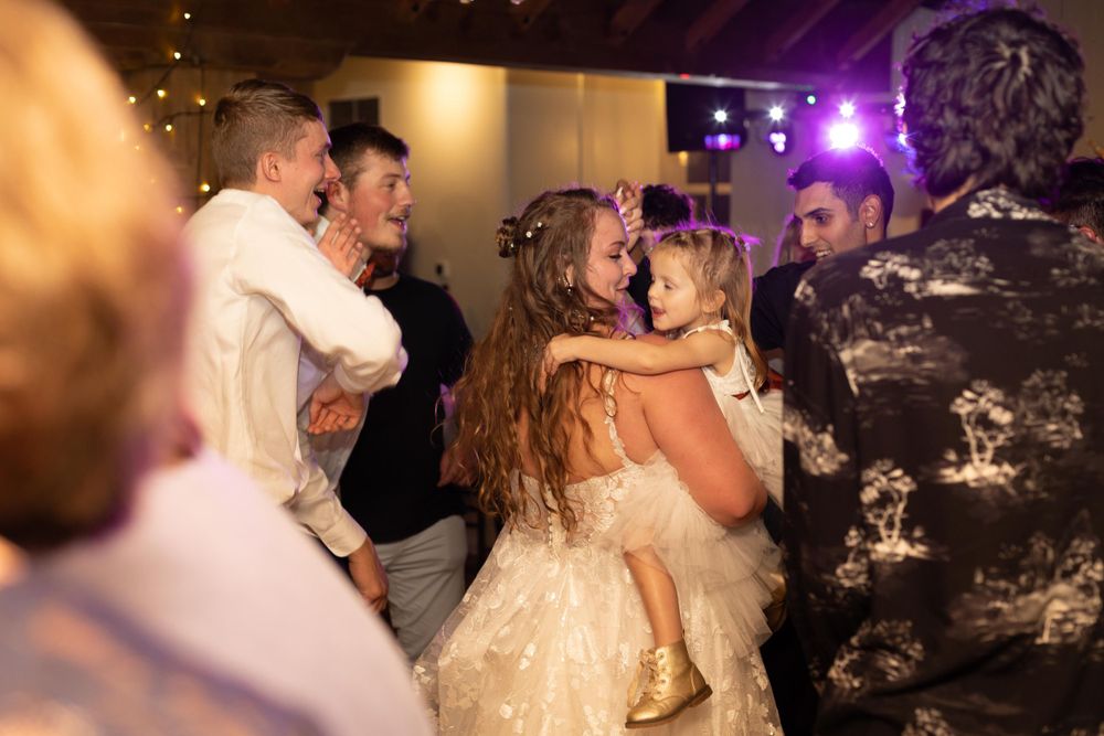 Wedding reception dance floor filled with celebratory guests under purple lighting.