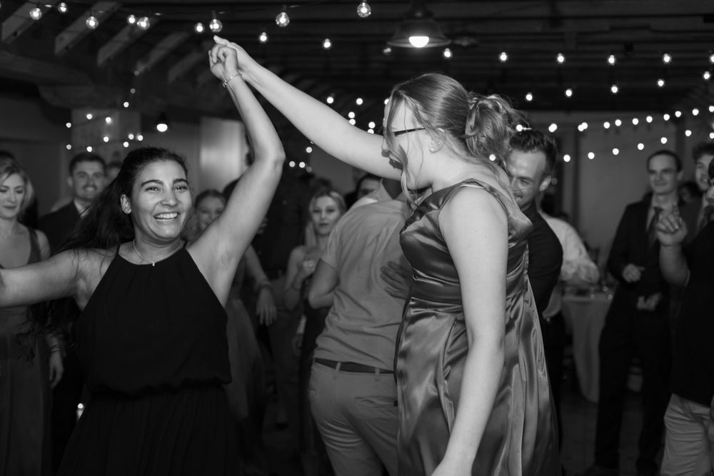 Wedding guests dancing joyfully under string lights at an indoor reception.