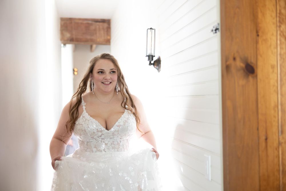 A lace wedding dress with delicate details shimmers in bright natural light from a hallway window.