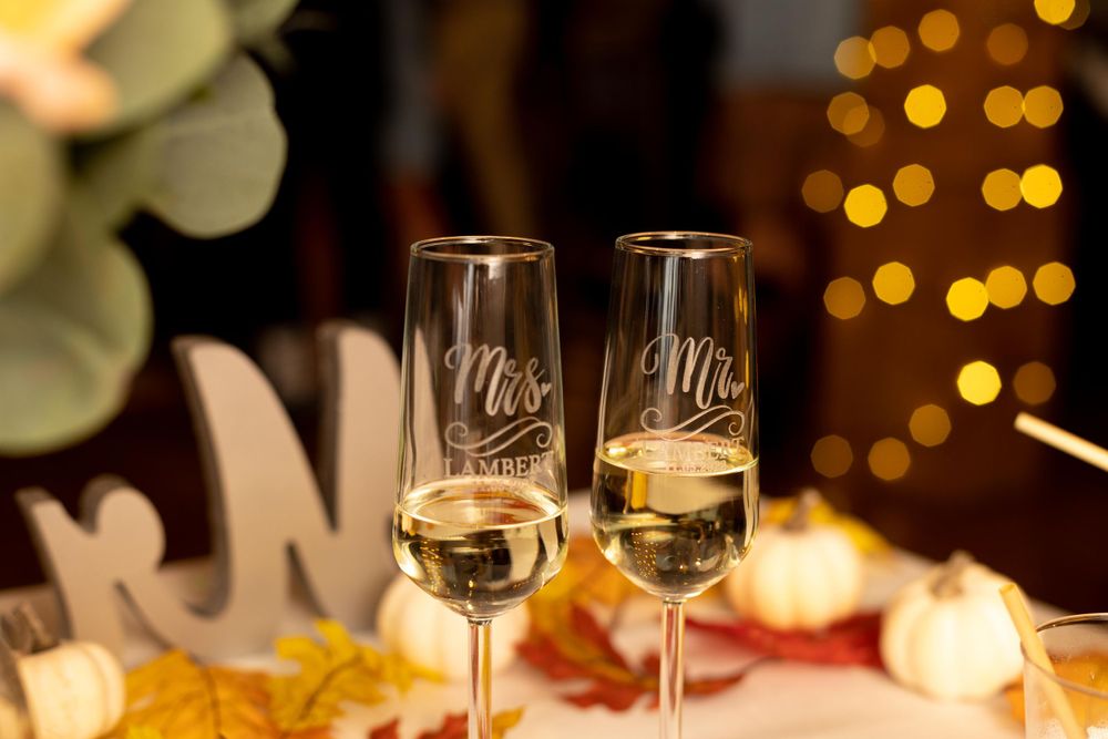 Two champagne flutes with 'Mr' and 'Mrs' etched on them against bokeh lights.