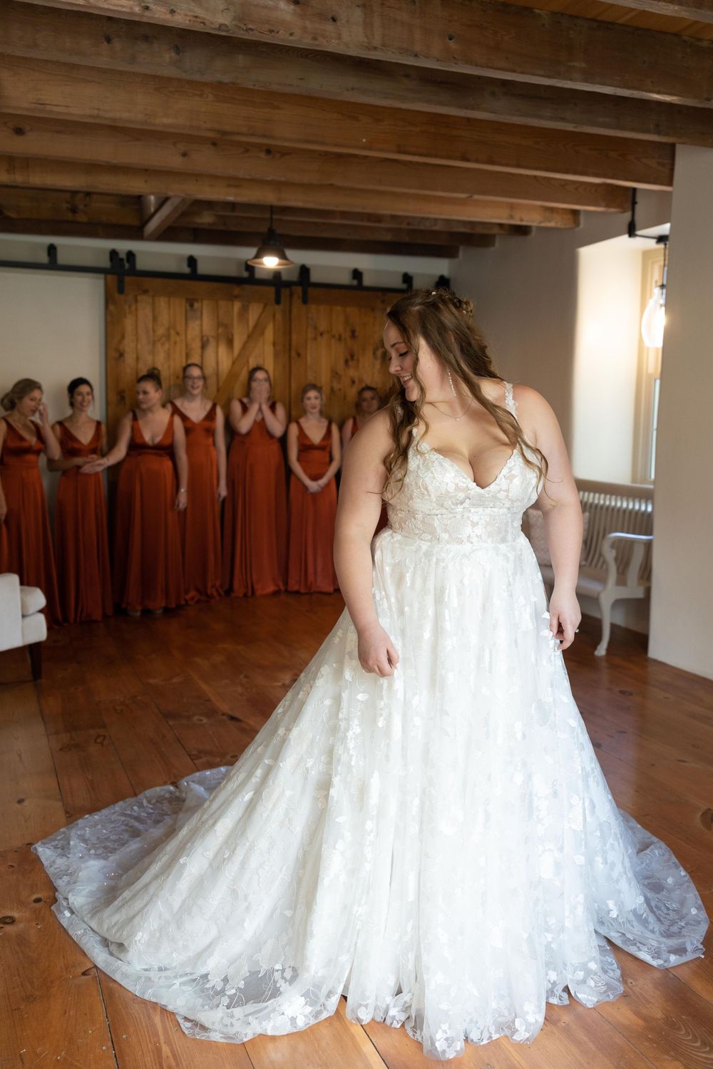 A stunning lace wedding gown with flowing train is showcased in a rustic room with wooden beams.