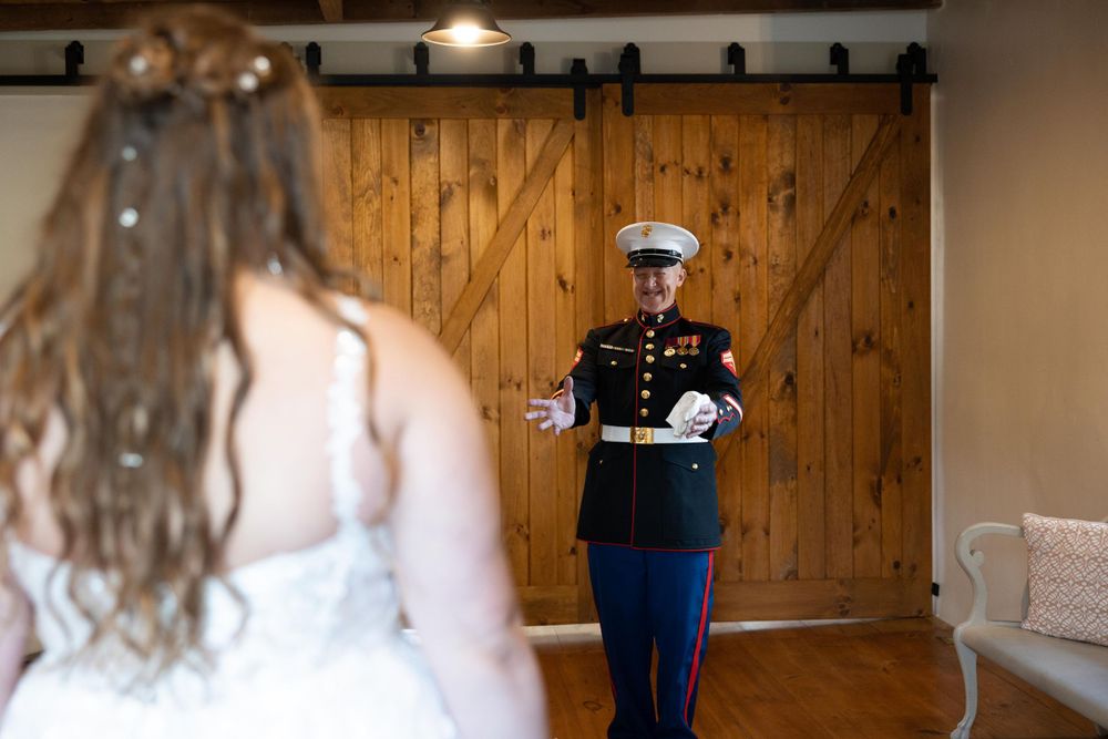 A Marine in dress blues uniform shares a first look moment with bride in front of rustic wooden barn doors.
