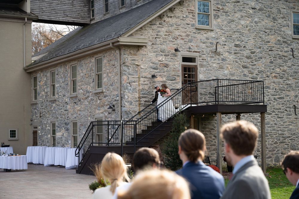 Wedding ceremony guests watch couple on stone building balcony during autumn outdoor event.