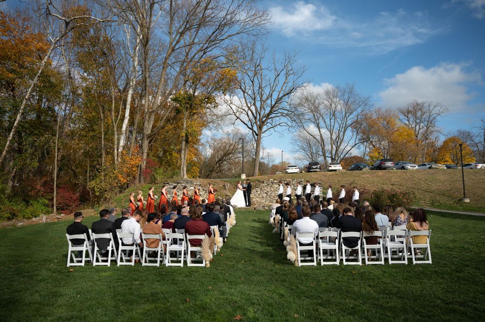 Aerial view of outdoor wedding ceremony setup with white chairs on lawn surrounded by autumn trees.