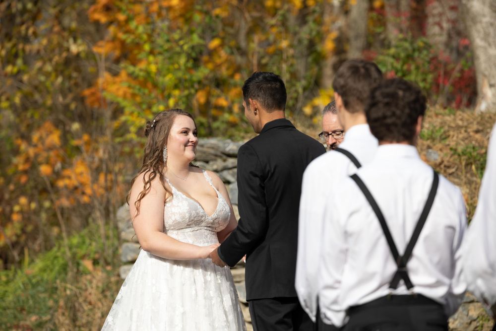 Wedding ceremony exchange of vows in front of autumn foliage backdrop.