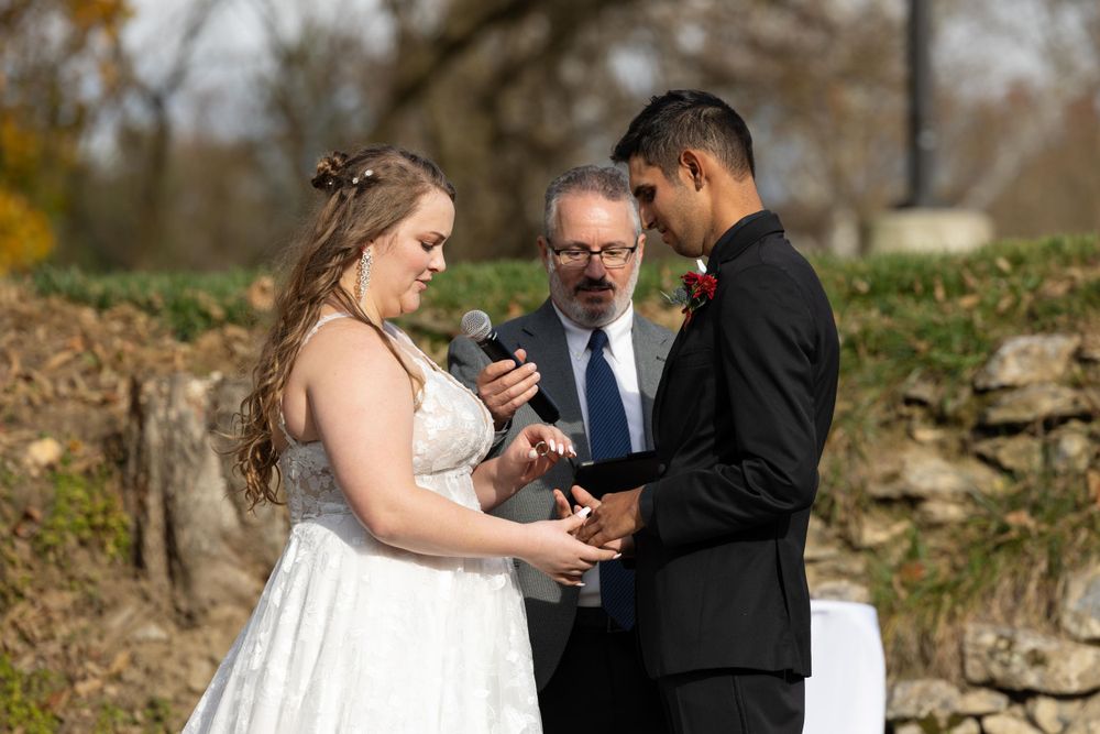 An intimate wedding ceremony moment unfolds against a rustic stone wall backdrop in autumn.