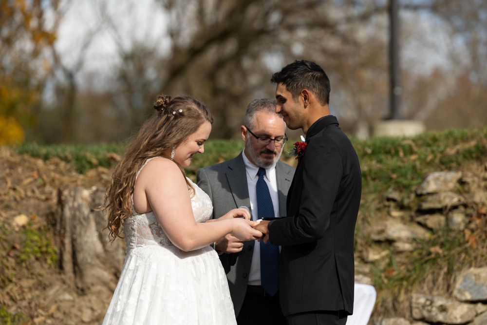 A wedding exchange of rings takes place during an outdoor autumn ceremony.