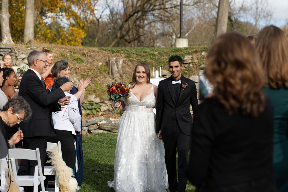 Wedding guests applaud during a recessional at an outdoor autumn ceremony.