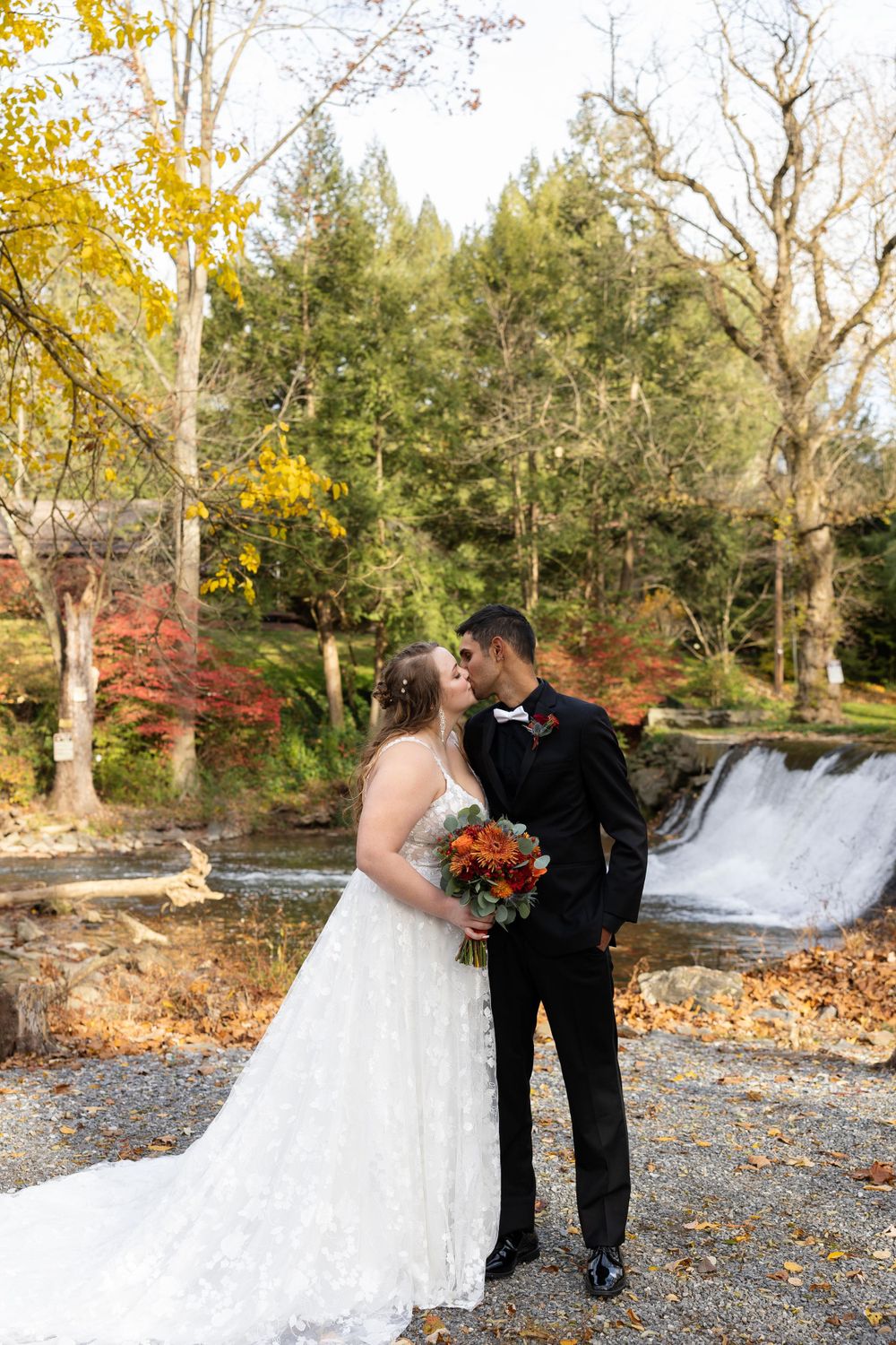 A romantic wedding portrait captured in front of a cascading waterfall with fall colors in the background.
