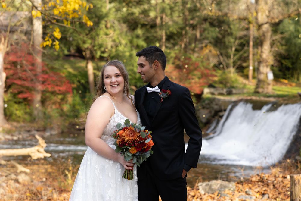 A couple poses for a romantic autumn wedding photo in front of a cascading waterfall with fall foliage.