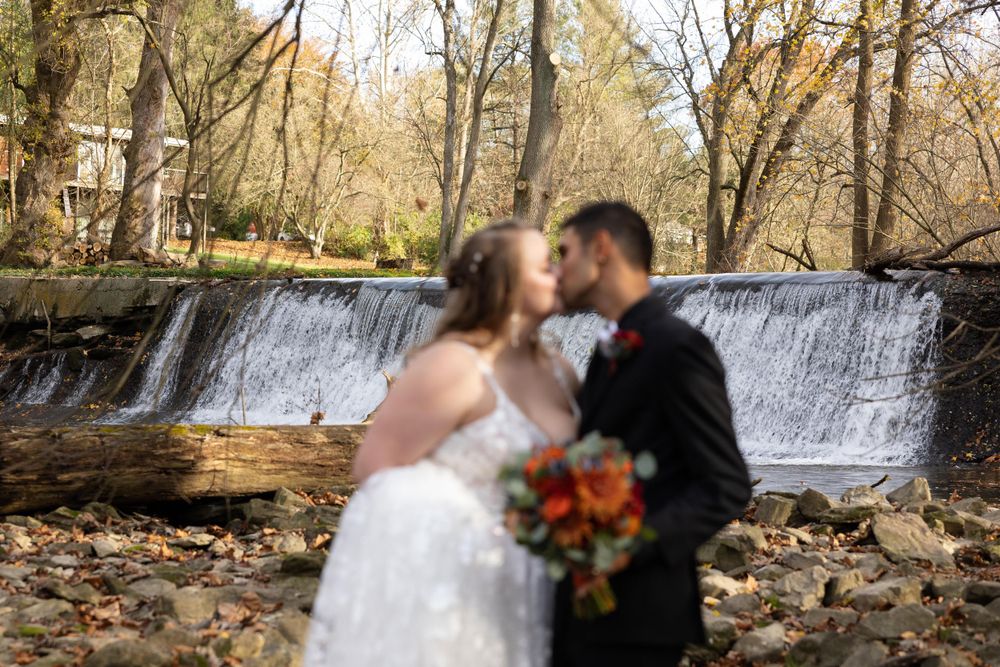 Wedding couple shares an intimate moment by a waterfall surrounded by autumn leaves.