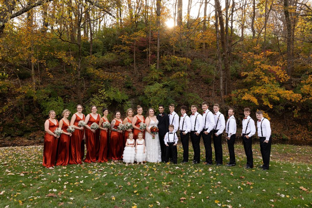 Wedding party in burgundy and white poses together against a backdrop of fall foliage.