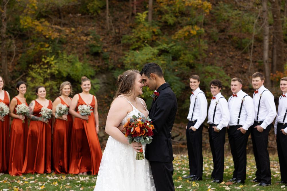 Wedding party in burgundy dresses and black suits stands in formation during an autumn ceremony.