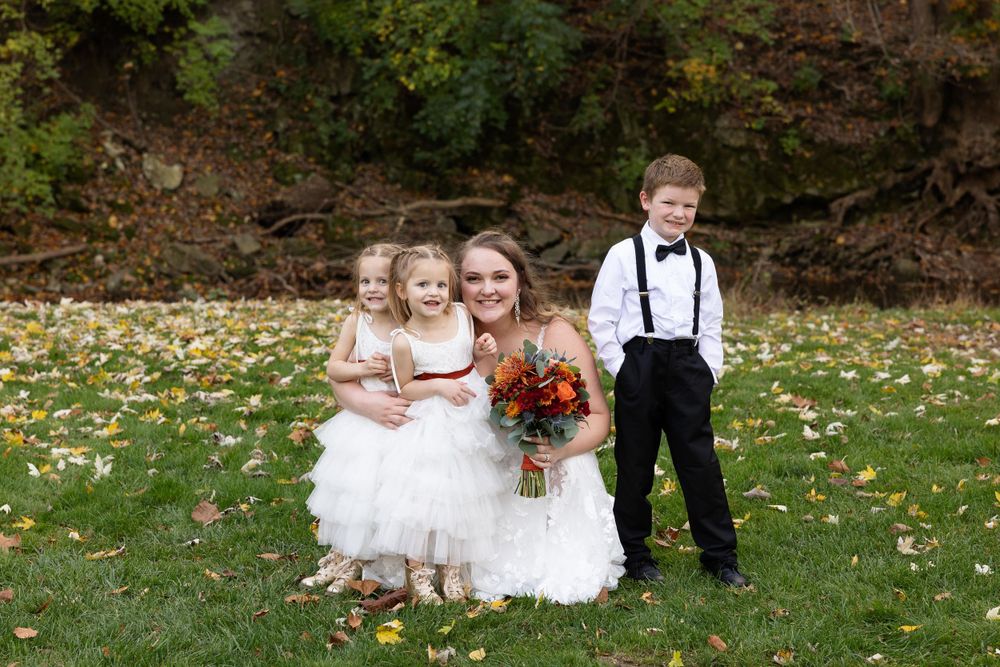 Wedding portrait with flower girls in white dresses and a young ring bearer in suspenders.