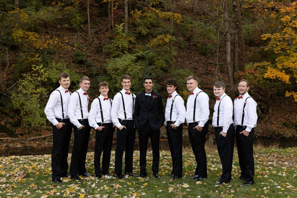 Groomsmen in black and white attire pose against colorful fall forest backdrop.