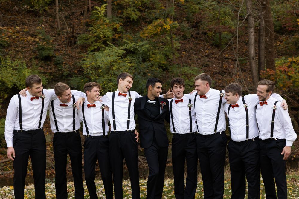 Formal group in black attire with suspenders pose casually against autumn forest.