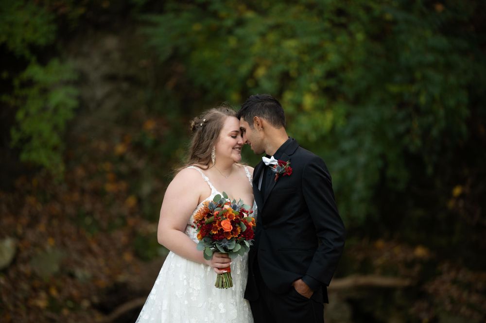 Newlyweds share intimate moment with autumn foliage in background, bride holding orange bouquet.