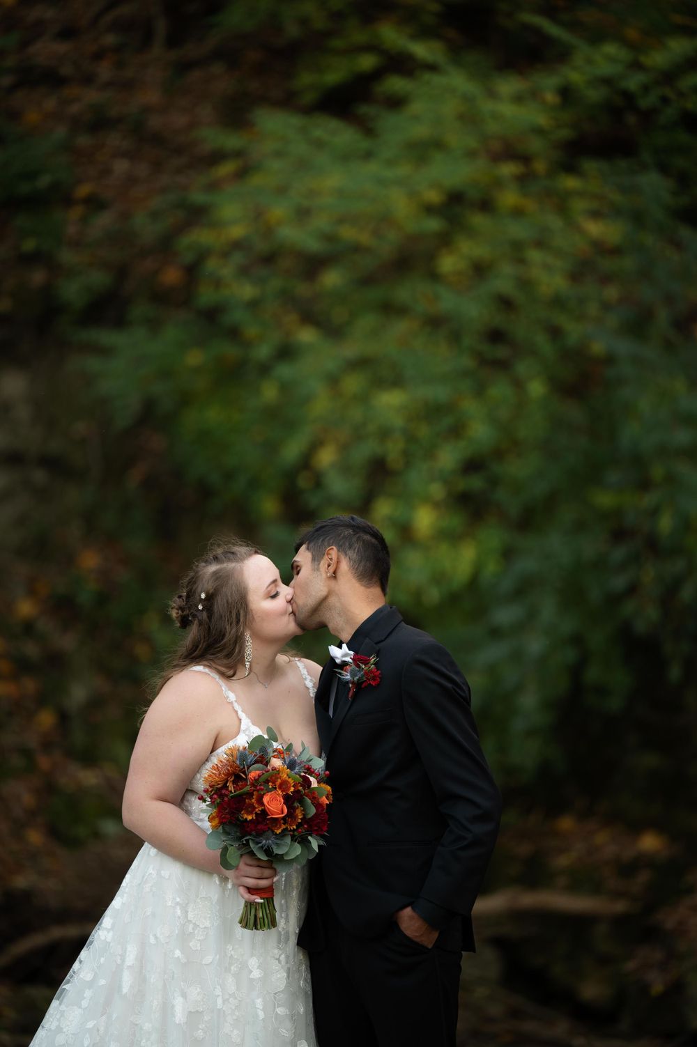 Wedding couple embraces in romantic moment with fall foliage and orange bouquet.
