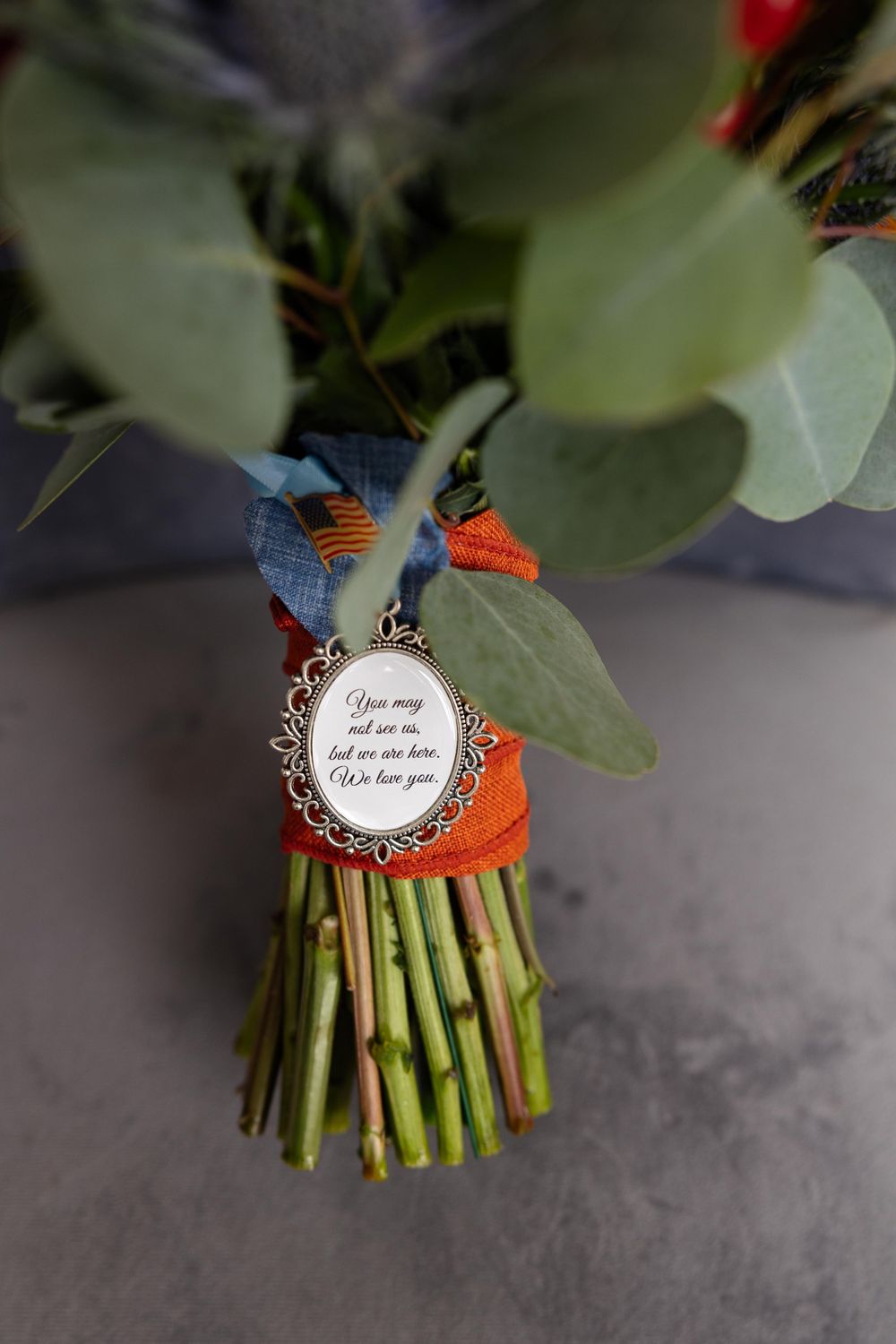 Close-up of wedding bouquet charm with blue ribbon and orange accent.