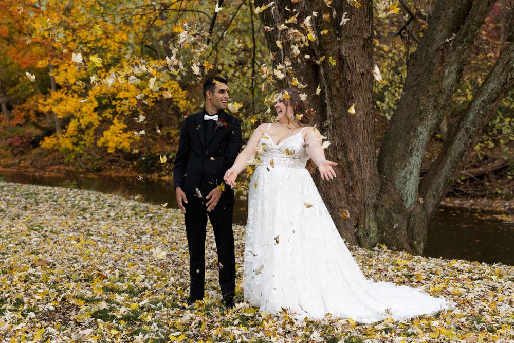 A couple stands together on fallen autumn leaves against a backdrop of golden trees.