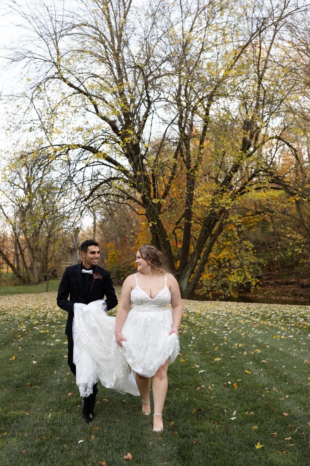 A couple walks together on grass with autumn trees in the background during their wedding.