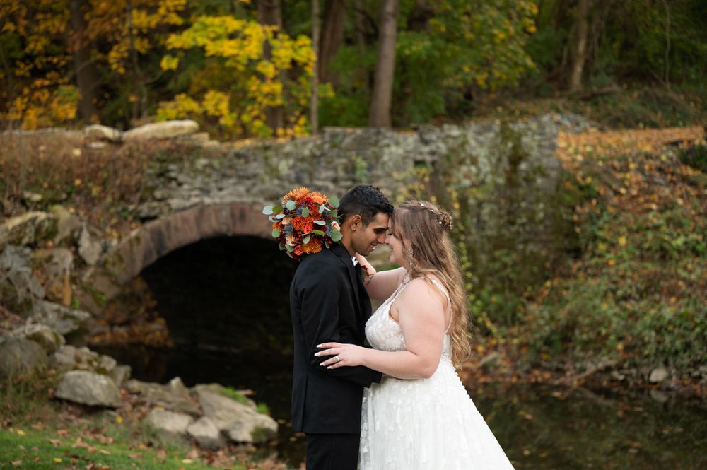 A couple embraces in front of a stone bridge during their fall wedding photoshoot.