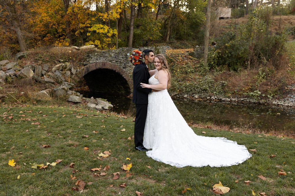 A couple poses for wedding photos in front of a rustic stone tunnel surrounded by fall foliage.