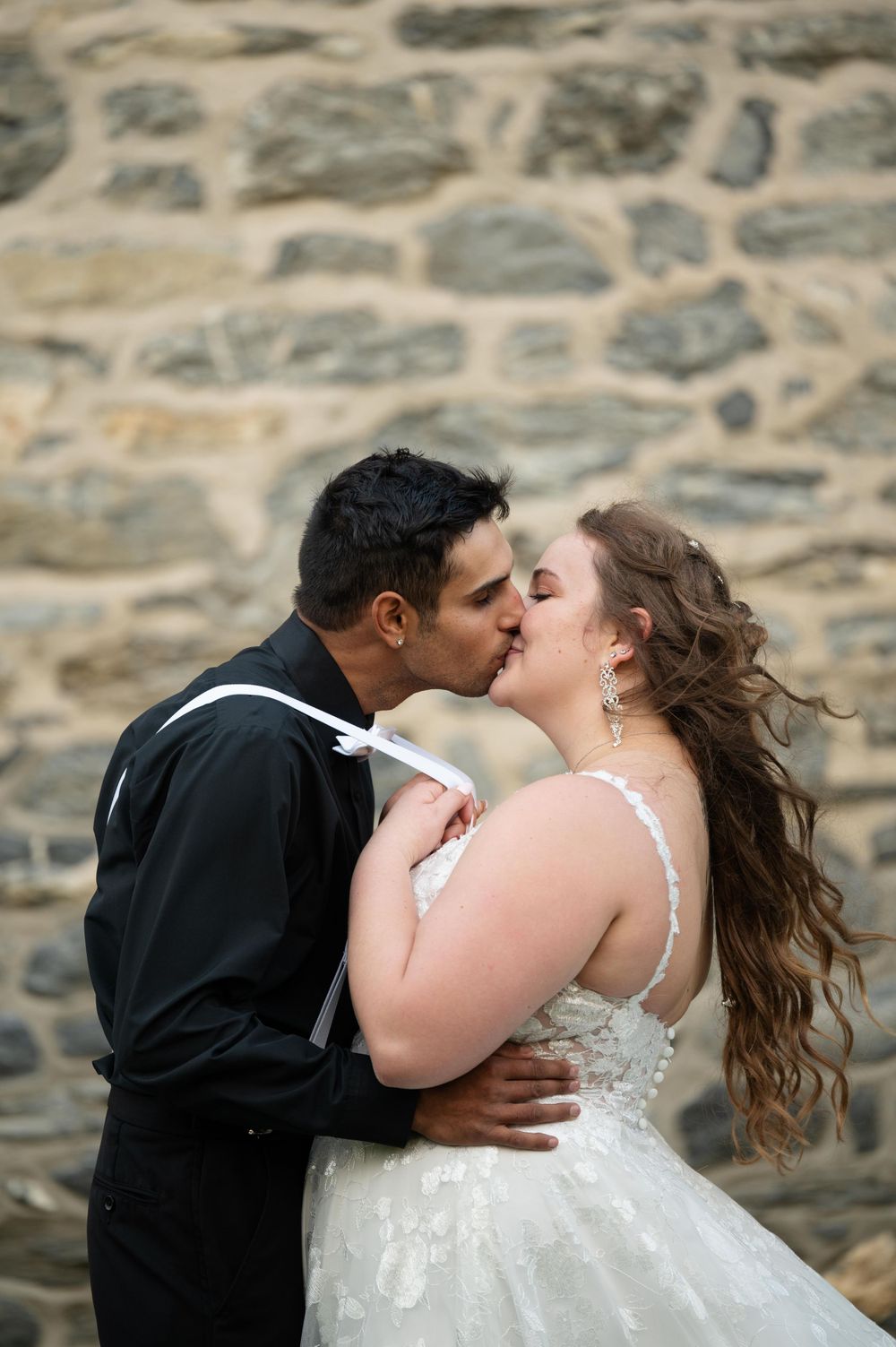A romantic wedding moment captured against a textured stone wall background.