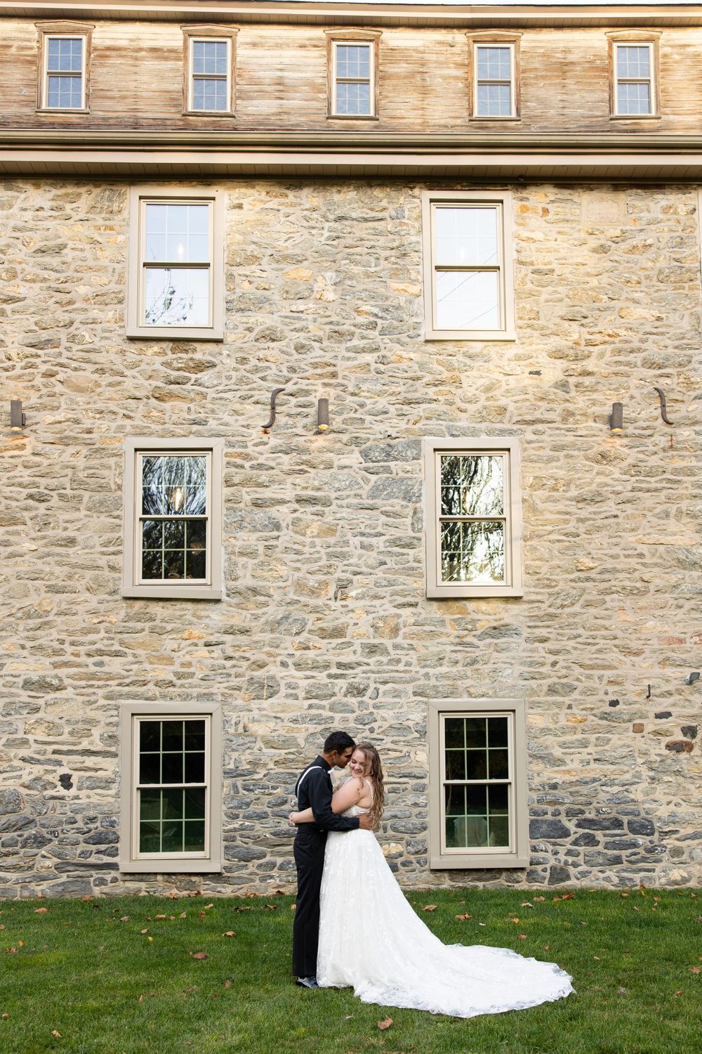 A couple shares an intimate moment against a historic stone building with symmetrical windows.