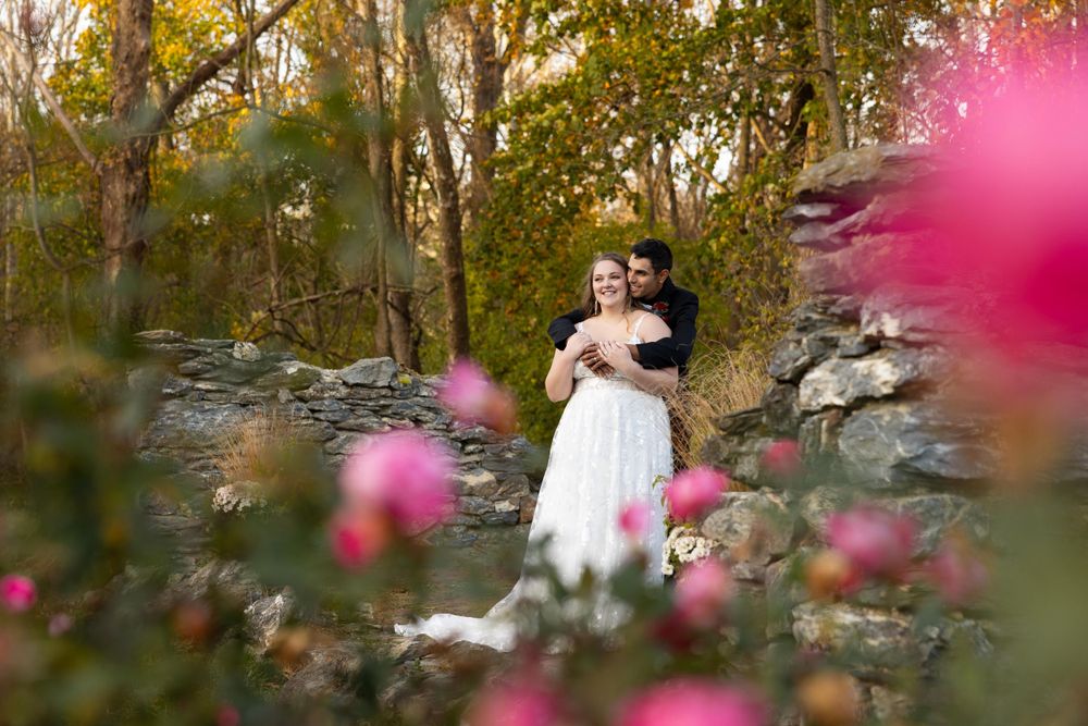 A couple embraces in an autumn garden setting with pink flowers in the foreground.