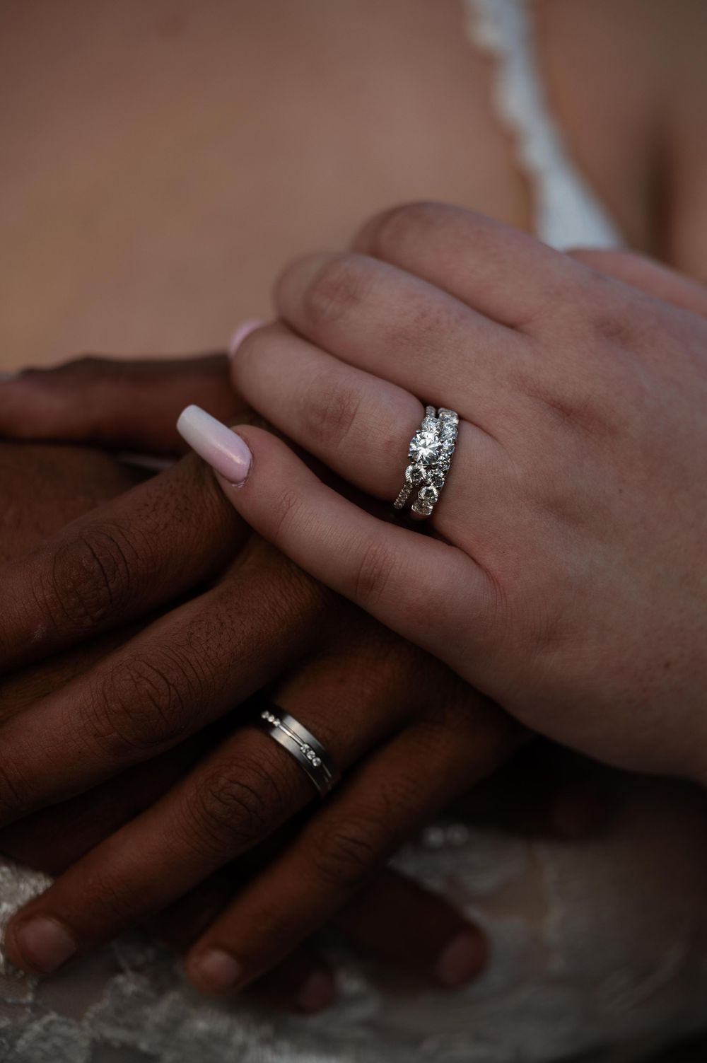 Wedding rings and hands intertwined showing both silver bands and a diamond engagement ring.