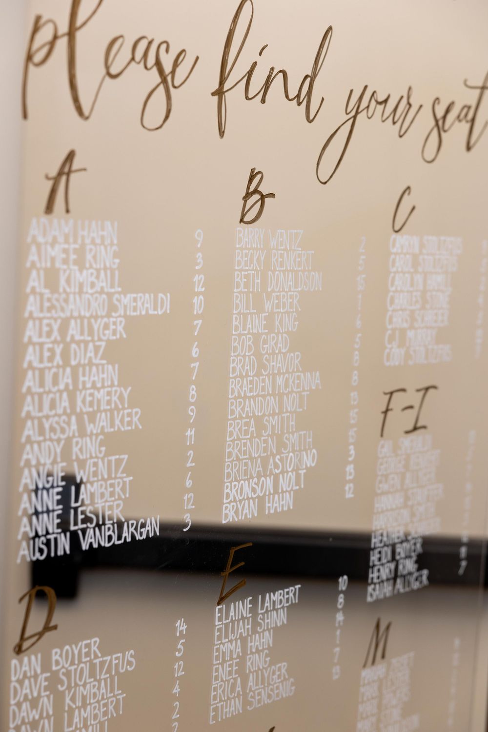 Elegant wedding seating chart display with alphabetically organized guest names in calligraphy on beige background.