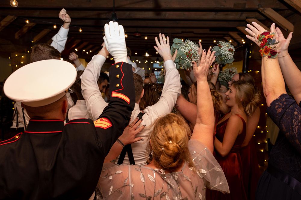Wedding guests dancing with raised hands under twinkling lights during reception celebration.