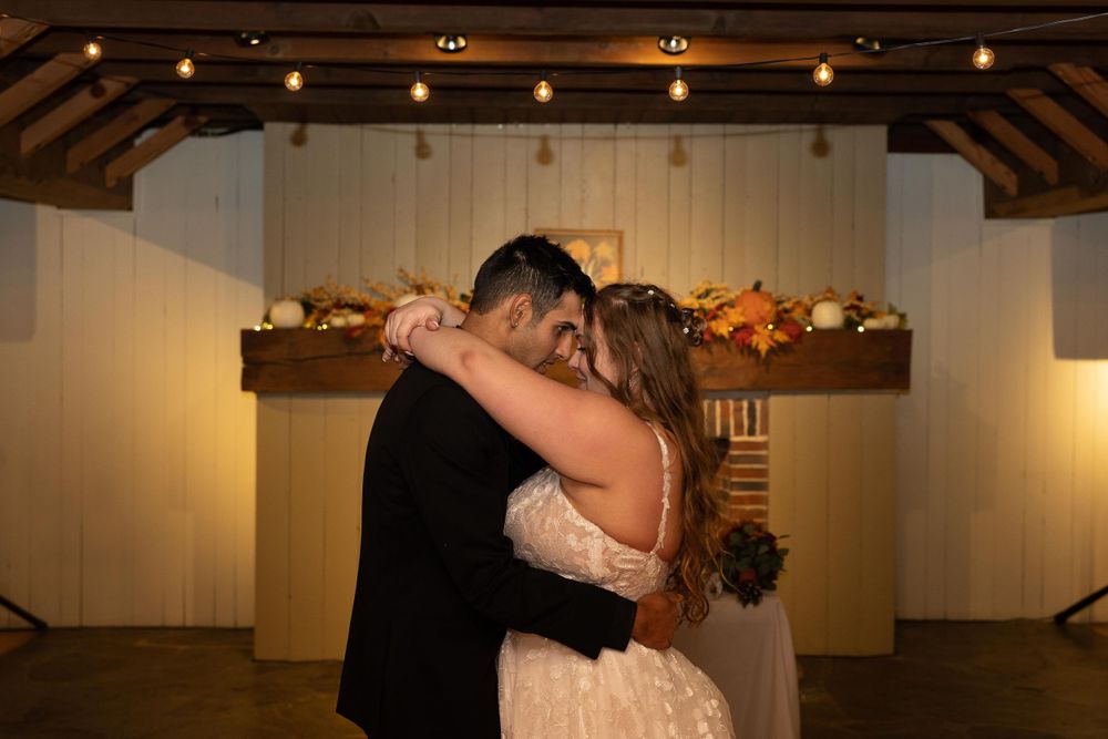 Romantic couple dancing in a warmly lit reception venue with string lights and wooden beams.